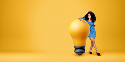 African woman showing thumb up standing near big light bulb on empty background
