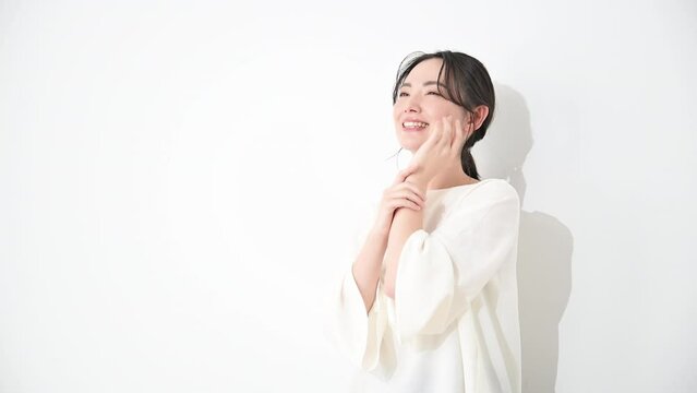 頬に手をあて笑顔のバストアップまとめ髪女性ビューティ　白背景の動画