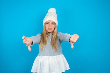 beautiful caucasian teen girl wearing grey sweater being upset showing thumb down with two hands....