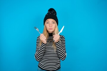 hungry beautiful caucasian teen girl wearing striped sweater holding in hand fork knife want tasty...