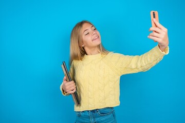 beautiful caucasian teen girl wearing yellow sweater  smiling and taking a selfie ready to post it...