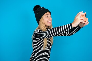 beautiful caucasian teen girl wearing striped sweater taking a selfie to post it on social media or...