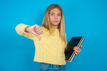 beautiful caucasian teen girl wearing yellow sweater looking unhappy and angry showing rejection and negative with thumbs down gesture. Bad expression.