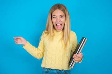beautiful caucasian teen girl wearing yellow sweater points aside on copy blank space. People promotion and advertising concept