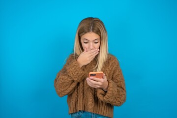 beautiful teen girl being deeply surprised, stares at smartphone display, reads shocking news on...