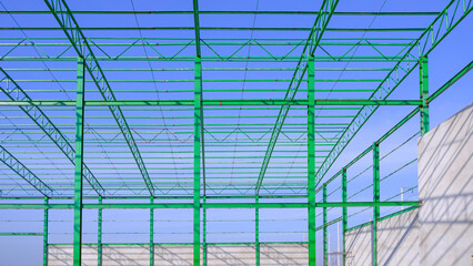 Metal roof beam and columns of new industrial warehouse building outline structure in construction area against blue sky background