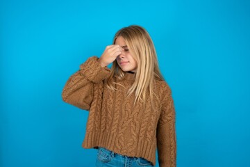 Sad beautiful caucasian teen girl wearing brown sweater suffering from headache holding hand on her...