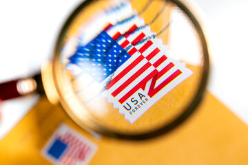 A postage stamp with an USA flag in an envelope under a magnifying glass on white background