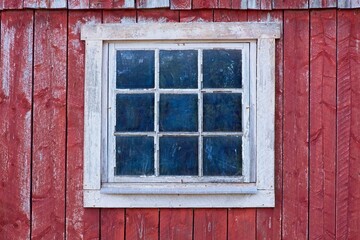 Closeup of a white framed window on a red painted old wooden building.