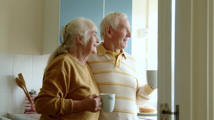 Happy senior couple drinking coffee or tea on home kitchen - 700595577