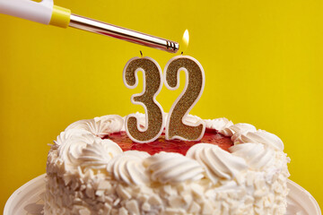 A candle in the form of the number 32, stuck in a festive cake, is lit. Celebrating a birthday or a...