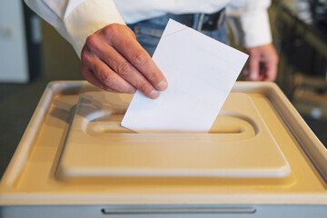 Voting in the Polling Station: Close-up of a man's hand putting his ballot into the ballot box,...