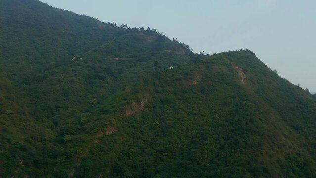 Couple of houses beside a huge hill full of green trees and vegetation, houses in rural green nature