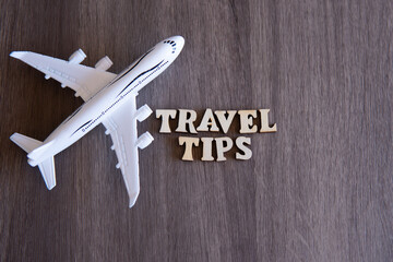 Toy plane and word TRAVEL TIPS on wooden table with copy space for text.