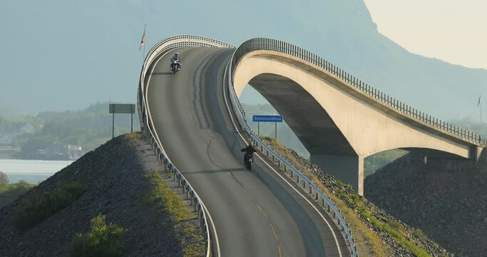 Two motorbikers ride along the Atlantic Ocean Road towards each other and greet each other.