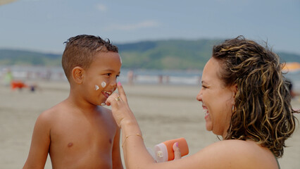 mother applying sunblock lotion on sons skin for sun protection little boy getting ready to swim on the beach with mom using sunscreen caring for childs health on sunny day