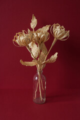A glass vase with a bouquet of flowers made from straw on the red background.