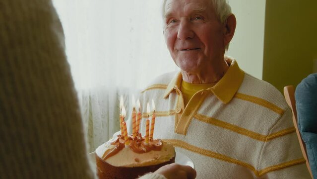 Old man looking at birthday cake and blowing candles