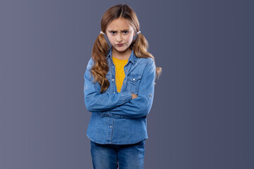 Sad and unhappy teenage girl. Schoolgirl 10 years old in a denim shirt and a yellow blouse on a gray background.
