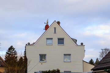 A white house with a red satellite dish and exterior panelling on a plot with trees and a road in...