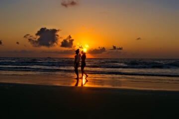 Fototapeta na wymiar Two women walking along shore at sunrise