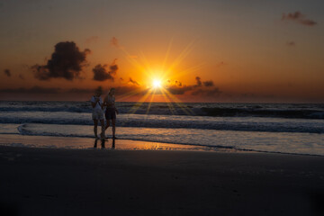 Two women enjoying walking along beach at sunrise