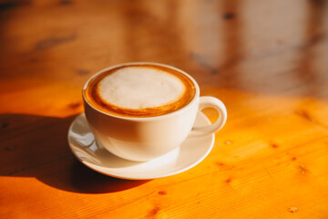 Coffee in white cup on wooden table, with spoon.