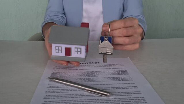 Key and model of house are in hands of female manager and contract document. Buying and selling real estate and credit and mortgage concept