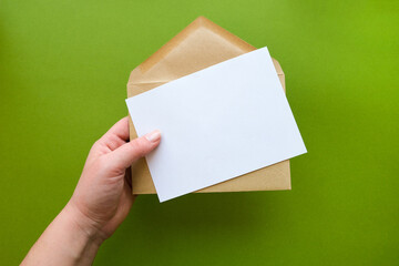 A hand holds a envelope with a blank sheet of paper. Letter template on green background