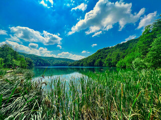 Piękne jezioro w górach w słoneczny letni dzień z błękitnym niebem, Jeziora Plitwickie w Chorwacji - obrazy, fototapety, plakaty