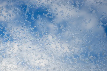 glass of roof window with frosted snowflakes and blue sky with clouds behind