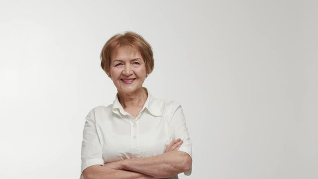 An elderly businesswoman crosses arms over chest, turns to the side with a condescending gaze, raises eyebrows, smiles and laughs. A joyful lady shows reaction to a funny thing. Demonstration of