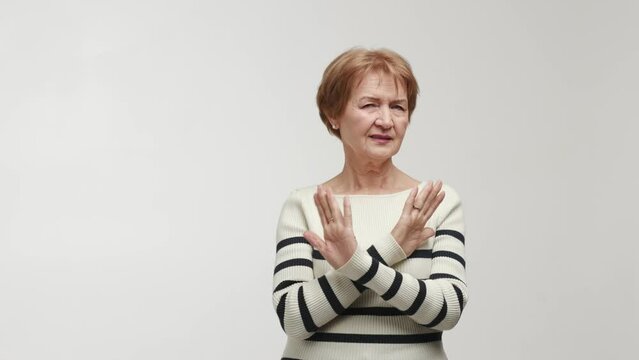 An elderly woman pulls a face with contempt and disgust, shows emotions of discontent, disapproval and inadmissibility. Gesture with crossed palms, sign of prohibition, categorical rejection