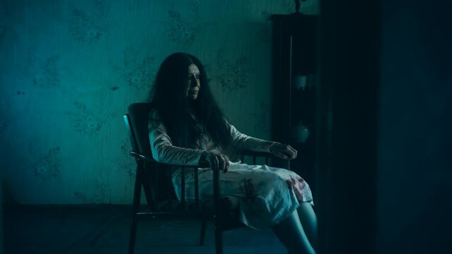 Spooky old witch in bloody gown sitting in armchair in haunted house, nightmare