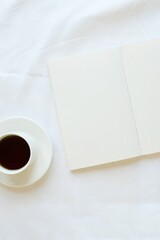 Opened note and coffee cup on a white sheet. Cozy composition on a bed