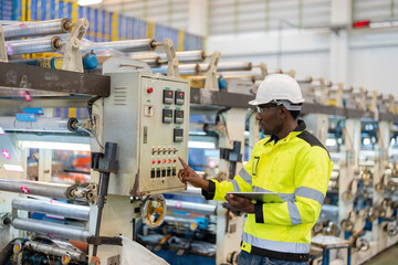 African male engineer Pressing buttons on electronic circuit boards, machinery of plastic and steel industries. Use a laptop to check company business systems. Wear a safety vest and helmet.