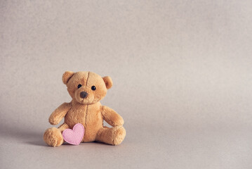 Small teddy bear with a pink heart on a beige background. Side view, selective focus, copy space. Valentine's Day.