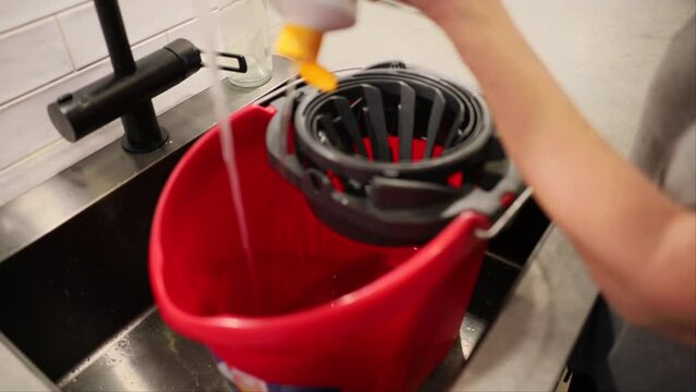 A bucket is filled with water in a sink to mop the floor. 