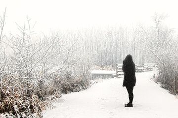 As snow falls around her, an unidentifiable woman pauses along a hiking trail to admire the view...