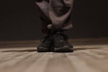 A Black fabric running shoe with grey jogger lower pants under spotlight by a man on wooden flooring, selective focused - obrazy, fototapety, plakaty