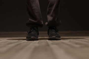 A Black fabric running shoe with grey jogger lower pants under spotlight by a man on wooden flooring, standing straight - obrazy, fototapety, plakaty