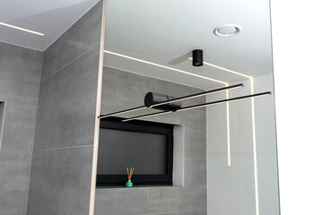 LED light strips mounted in the wall and ceiling in a modern bathroom, visible black wall lamp.