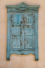 blue painted old wooden window with closed shutters on beige house wall