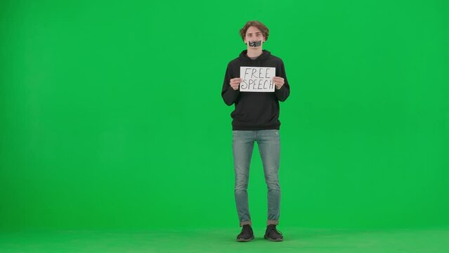 A man with his mouth taped with black tape holds a poster with the inscription Free speech. A Protestant man with a placard shrugs his shoulders in the studio on the green screen.