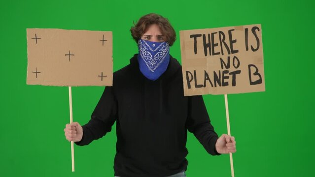 A male demonstrator with his face covered by a scarf holds up a sign that says There is no planet B and a blank sign. The man shouts slogans on a green screen close up. Chroma key.