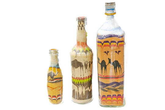 Three bottles full of sand. Colorful dromedary camels and sand dunes in the African Sahara desert made by sand drawing. Curves and patterns hand made with different colors of sand grains.