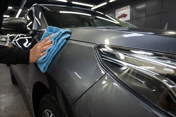 A man wipes the surface of the body of a gray car with a microfiber cloth. 