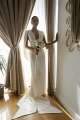 beautiful bride in elegant wedding dress and accessories posing in elegant hotel room