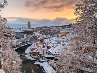 Winter view of Czech Krumlov. Český Krumlov, UNESCO. Historical town with Castle and Church at sunrise. Beautiful winter morning landscape with an illuminated monument. Snowy cityscape scene from the  - obrazy, fototapety, plakaty