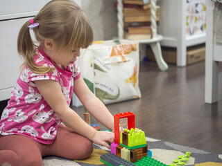 girl plays with construction kit at home on the floor, collect construction kit